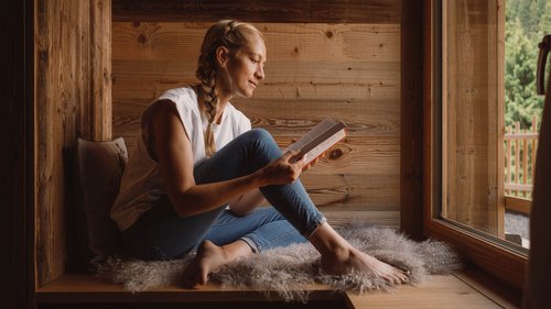 Erholungsurlaub im Chalet im Stubaital Frau sitzt entspannt am Fenster und liest ein Buch in einer Holzhütte