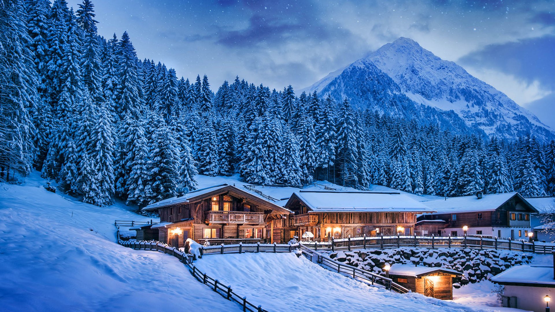 Erholungsurlaub im Chalet im Stubaital Verschneite Holzhütten vor einem bewaldeten Berg unter sternklarem Nachthimmel
